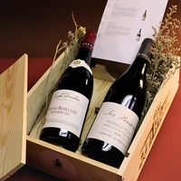 Two bottles of wine in a wooden crate with decorative plants.