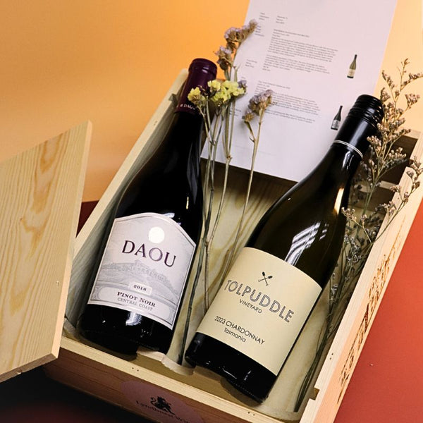 Two wine bottles, one labeled 'DAOU' and the other 'Wolpuddle', in a wooden box with flowers and a menu.