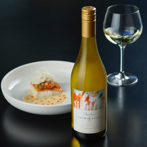 Bottle of Leuwin Estates white wine with a glass and plate of food on a dark background