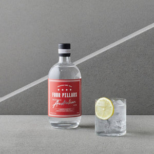 A bottle of Four Pillars Modern Australian Gin stands on a gray surface beside a clear glass filled with ice and a lemon slice,